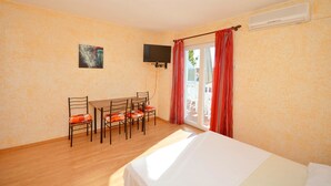 Una stanza con un letto, un tavolo con sedie, una televisione e una porta finestra con tende rosse.