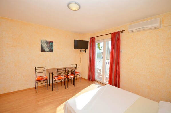 A room with a bed, a table with chairs, a TV, and a sliding glass door with red curtains.