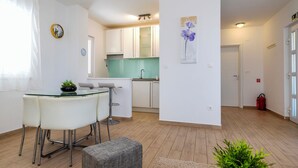 A modern kitchen with white cabinets, a green backsplash, and a dining area with a glass table and chairs. - House Goran (Kolan)