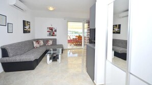 Una sala moderna con un sofá gris, una mesa de centro de vidrio y un comedor con mesa y sillas. Hay una puerta corrediza de vidrio que da a un balcón exterior.