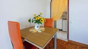 A dining area with a wooden table, orange chairs, a vase with sunflowers, and a kitchen visible through an archway. - Apartments Carmen (Kampor)