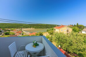Ein Balkon mit Tisch und Stühlen mit Blick auf einen Fluss und einen Hügel mit Gebäuden.
