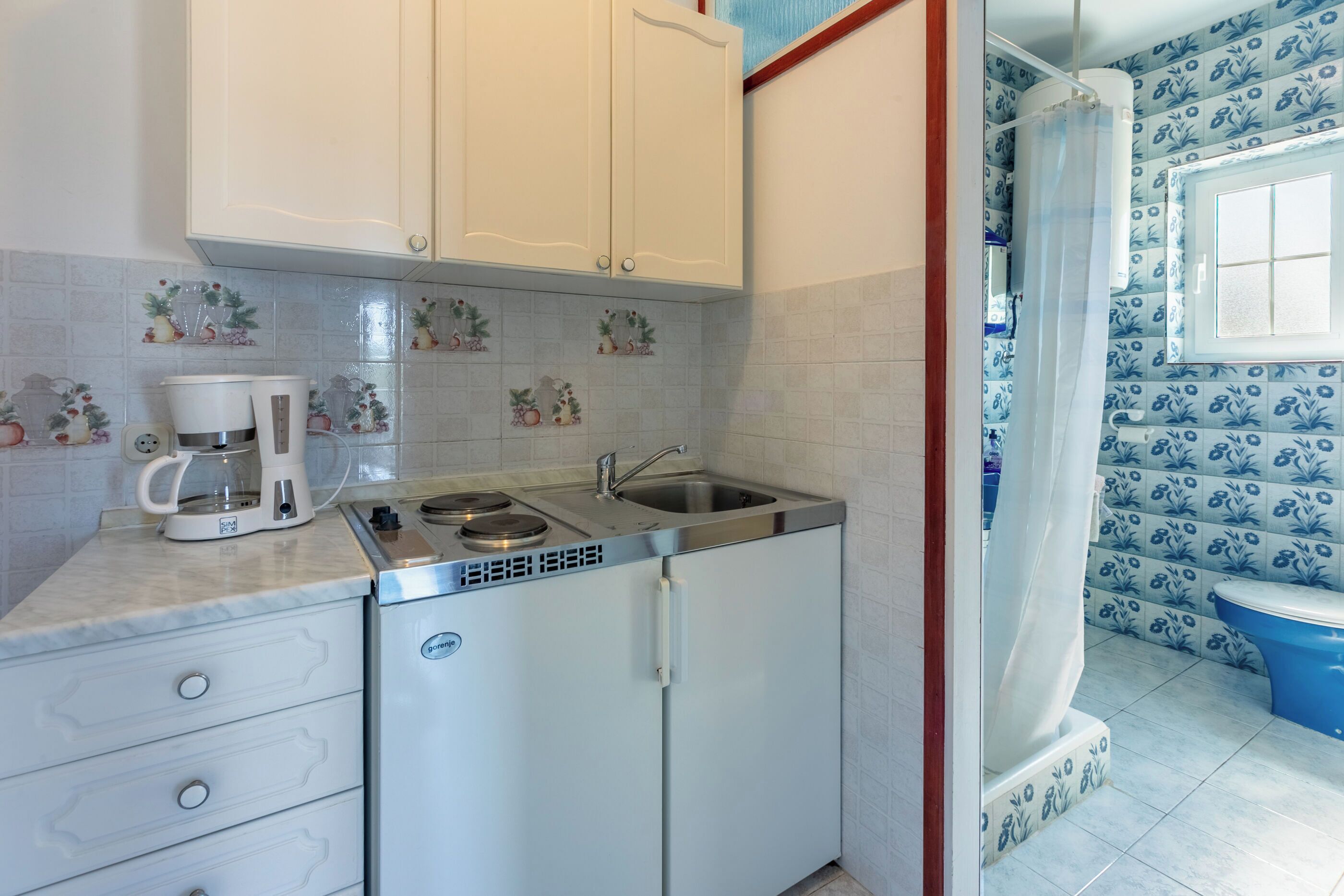 A compact kitchen with a built-in refrigerator, a coffee maker, and a sink.
