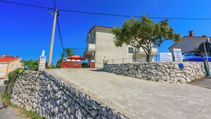 A stone wall, a building with a red umbrella, and a blue car. - Apartments Carmen (Kampor)