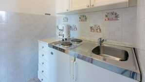 A compact kitchen with a built-in stove, a sink, and a white cabinet with a handle. - Apartments Carmen (Kampor)