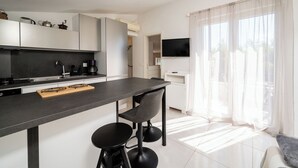 A modern kitchen with a central island, bar stools, a flat-screen TV, and a large window with sheer curtains. - Apartments Villa Bok (Okrug Gornji)