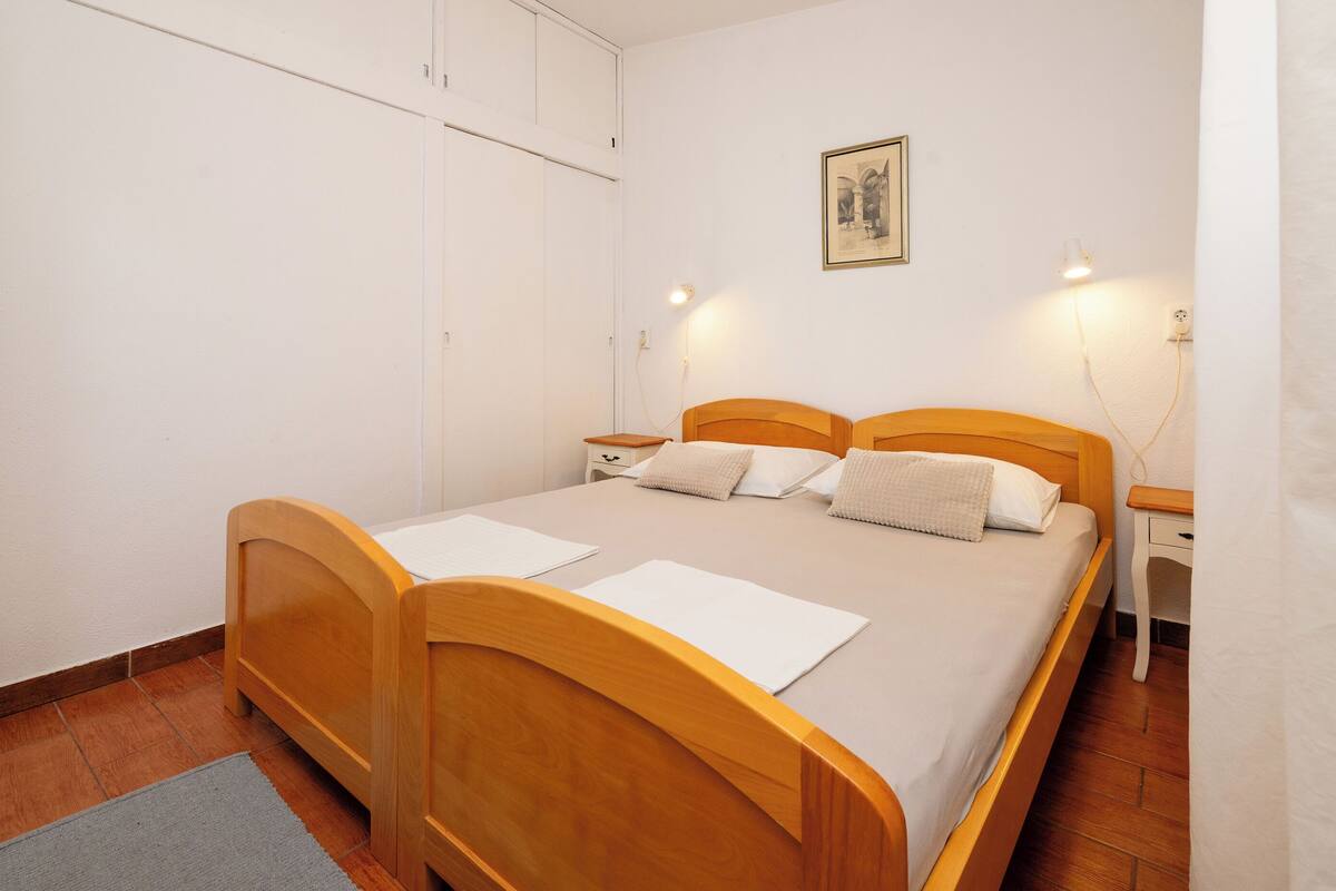 A bedroom with a wooden bed, white walls, a framed picture, and bedside lamps.