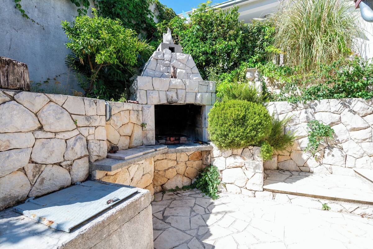 A stone-built outdoor kitchen area with a stone oven, surrounded by greenery and a stone wall.