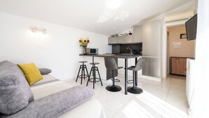 A compact living space with a sofa, a dining area with stools, a kitchen, and a TV mounted on the wall. - Apartments Villa Bok (Okrug Gornji)