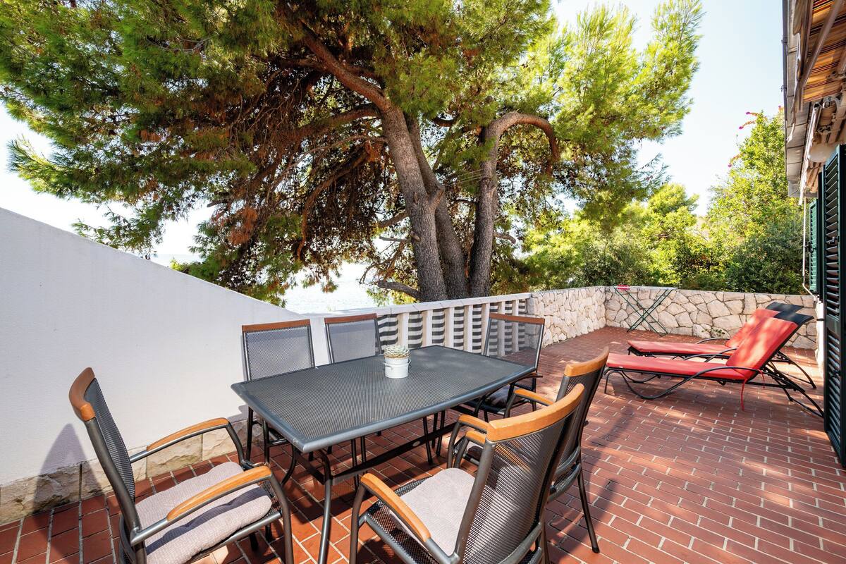 An outdoor patio with a table and chairs, a stone wall, and a tree.