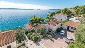 A coastal residential area with houses featuring red-tiled roofs, a parking area, and a view of the sea. - Apartments Villa Bok (Okrug Gornji)