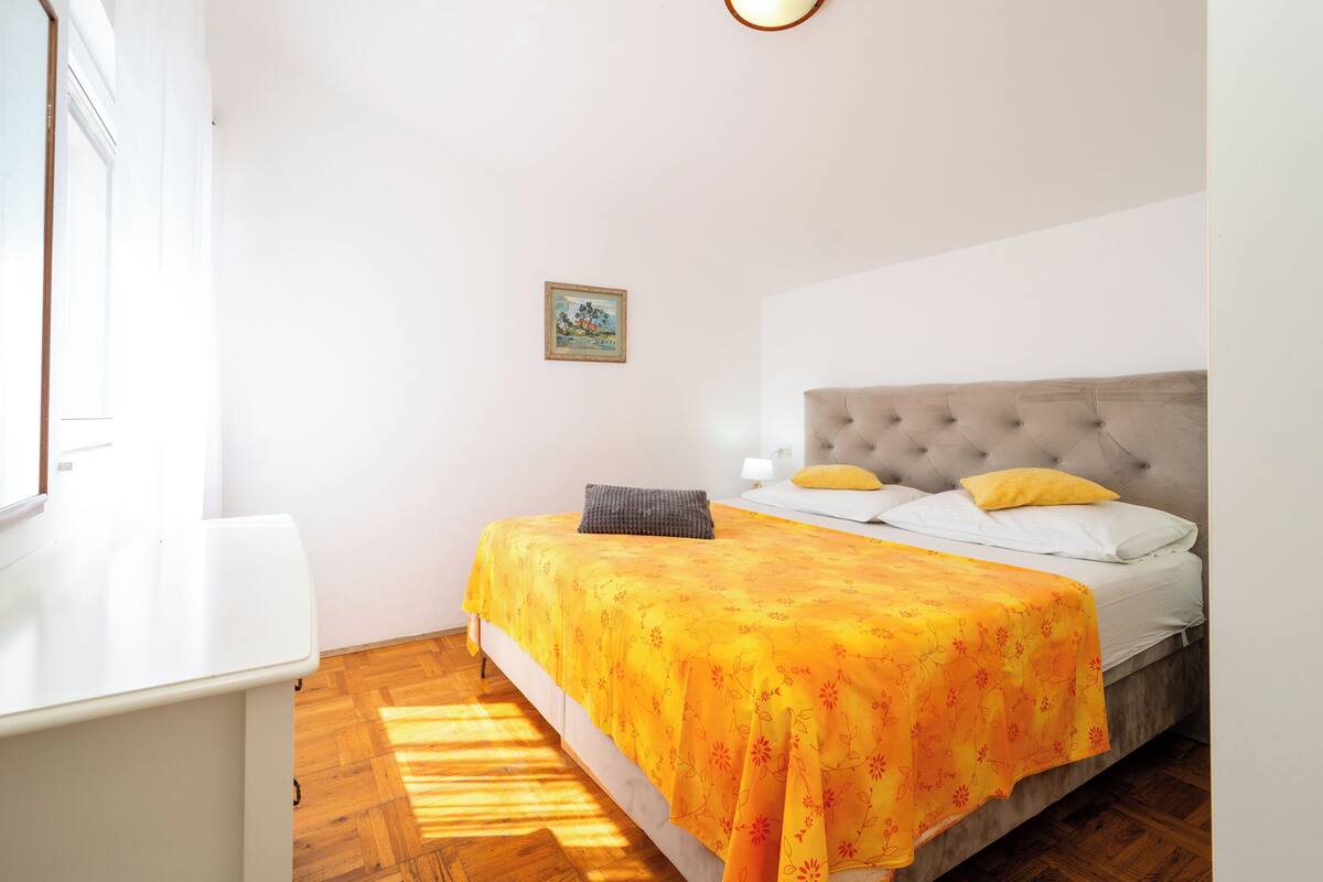 A bedroom with a bed, a bedside table, a window, and a picture on the wall.