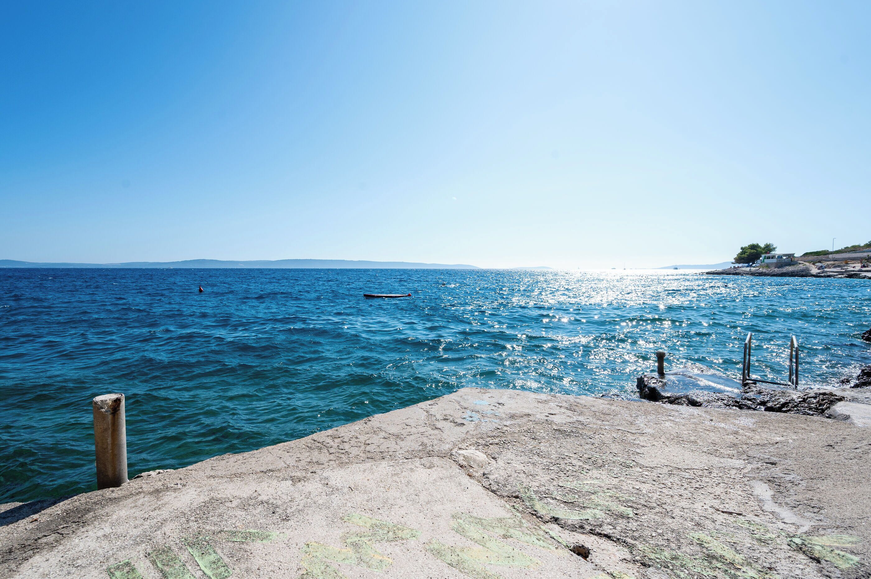 A coastal scene with a clear sky, calm sea, and rocky shoreline.