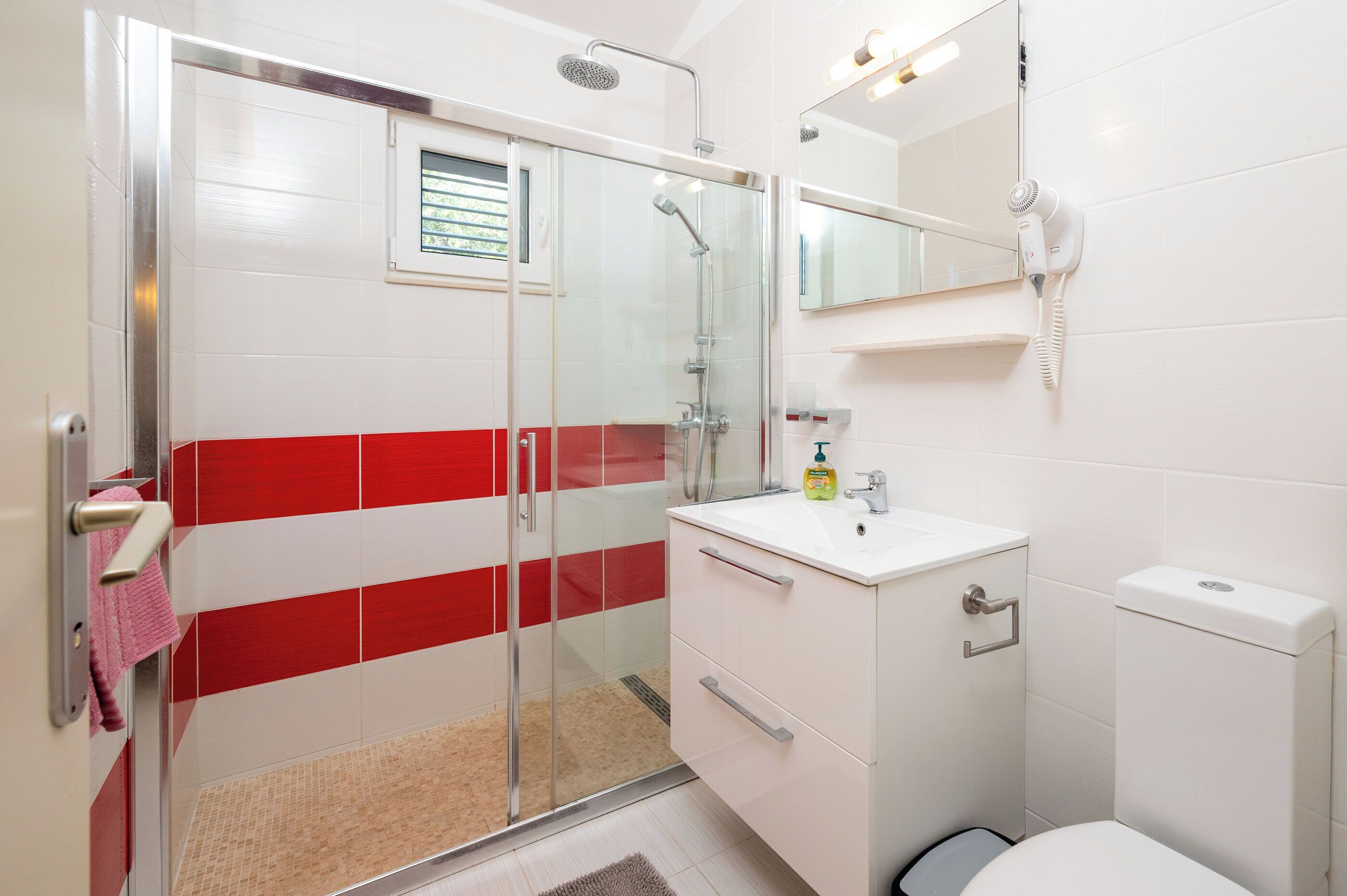 Une salle de bain avec une douche à parois de verre, un lavabo blanc avec un miroir au-dessus et des toilettes.