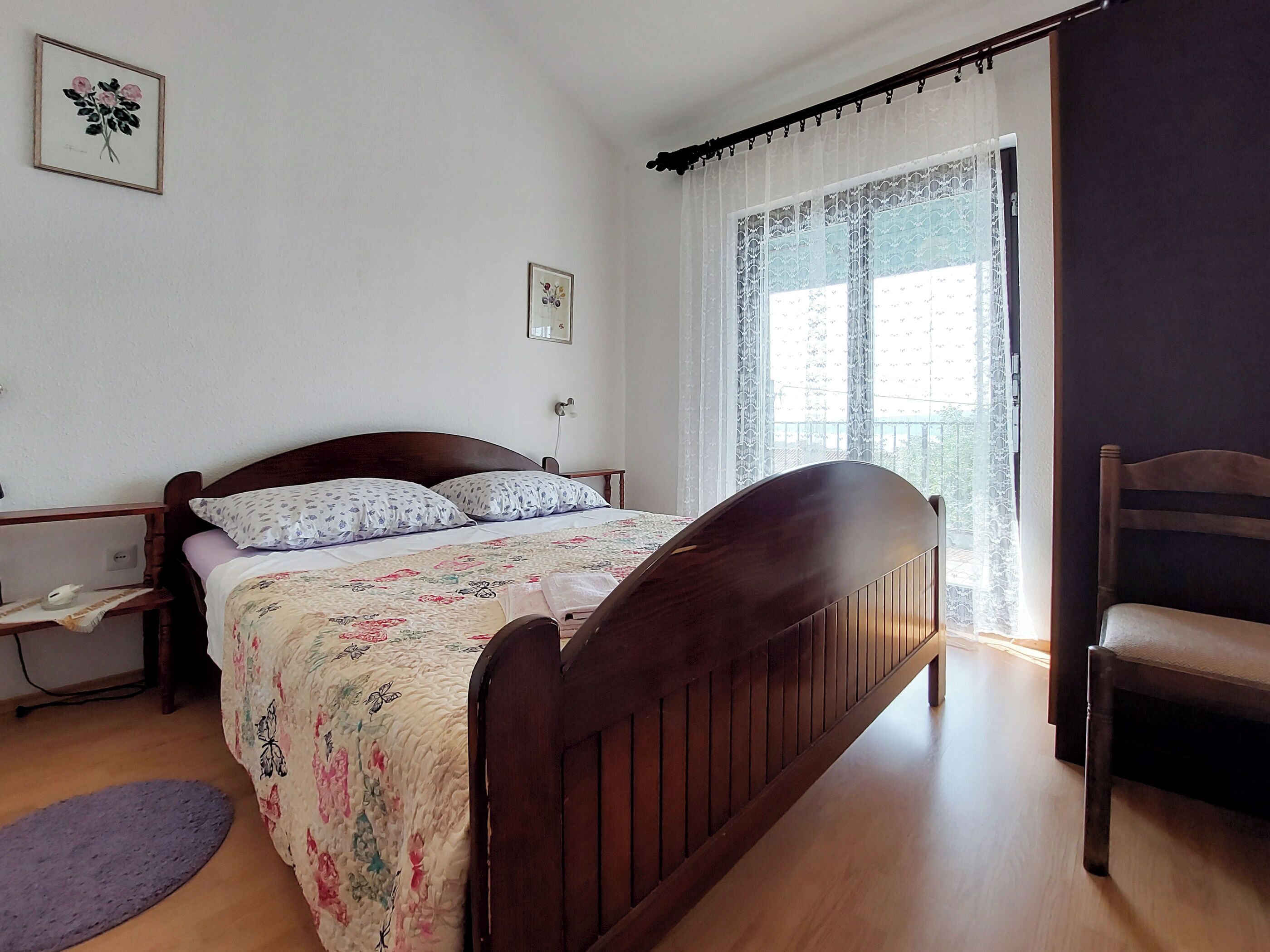 A bedroom with a wooden bed, a bedside table, a chair, and a window with curtains.