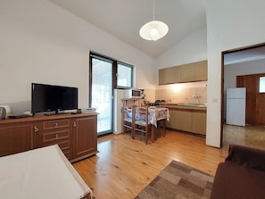 A compact kitchen with a dining area, wooden cabinets, a television, and a large window. - Apartments Vilim (Krk)