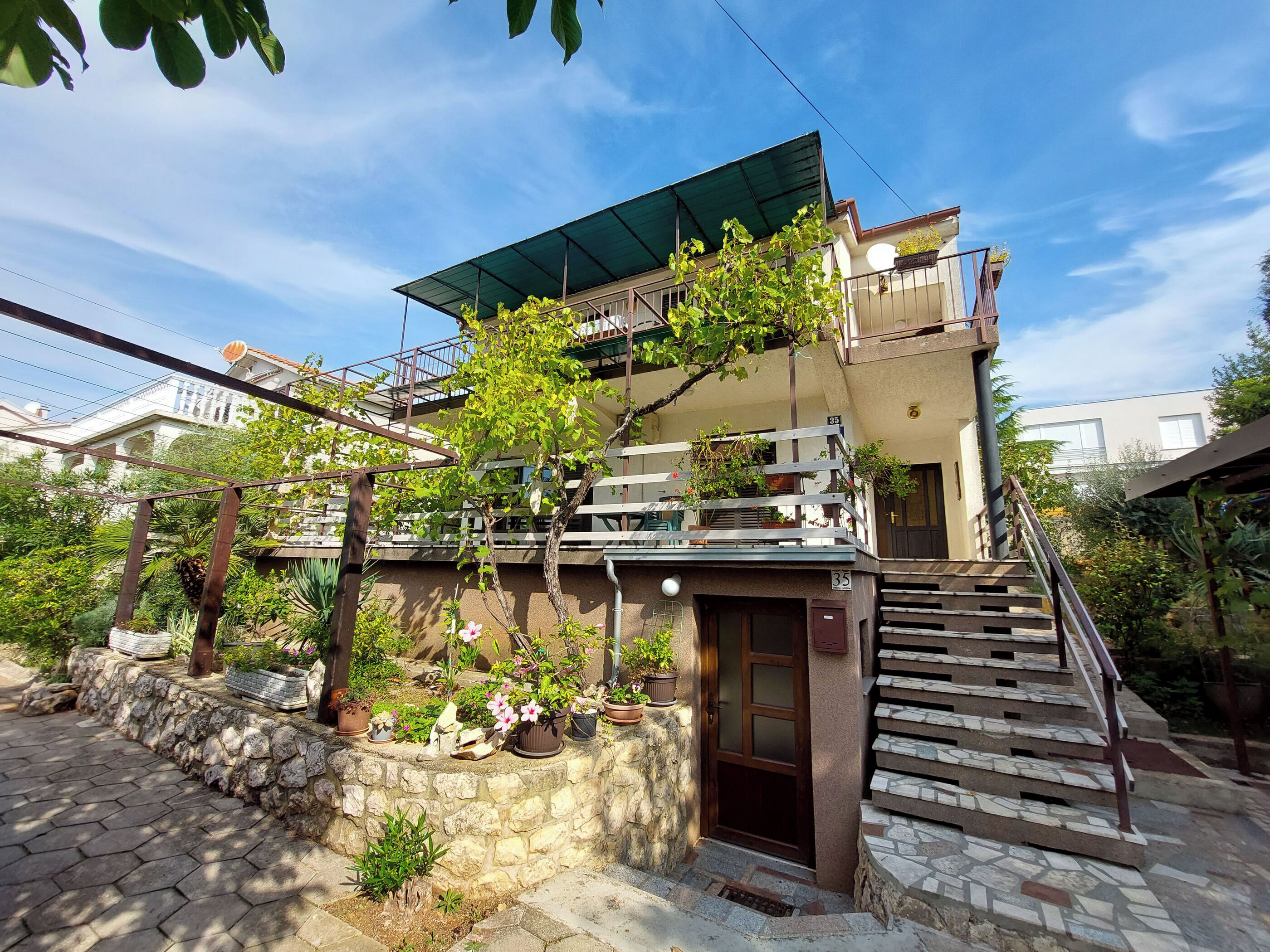 A two-story building with a balcony, stone steps, and potted plants.