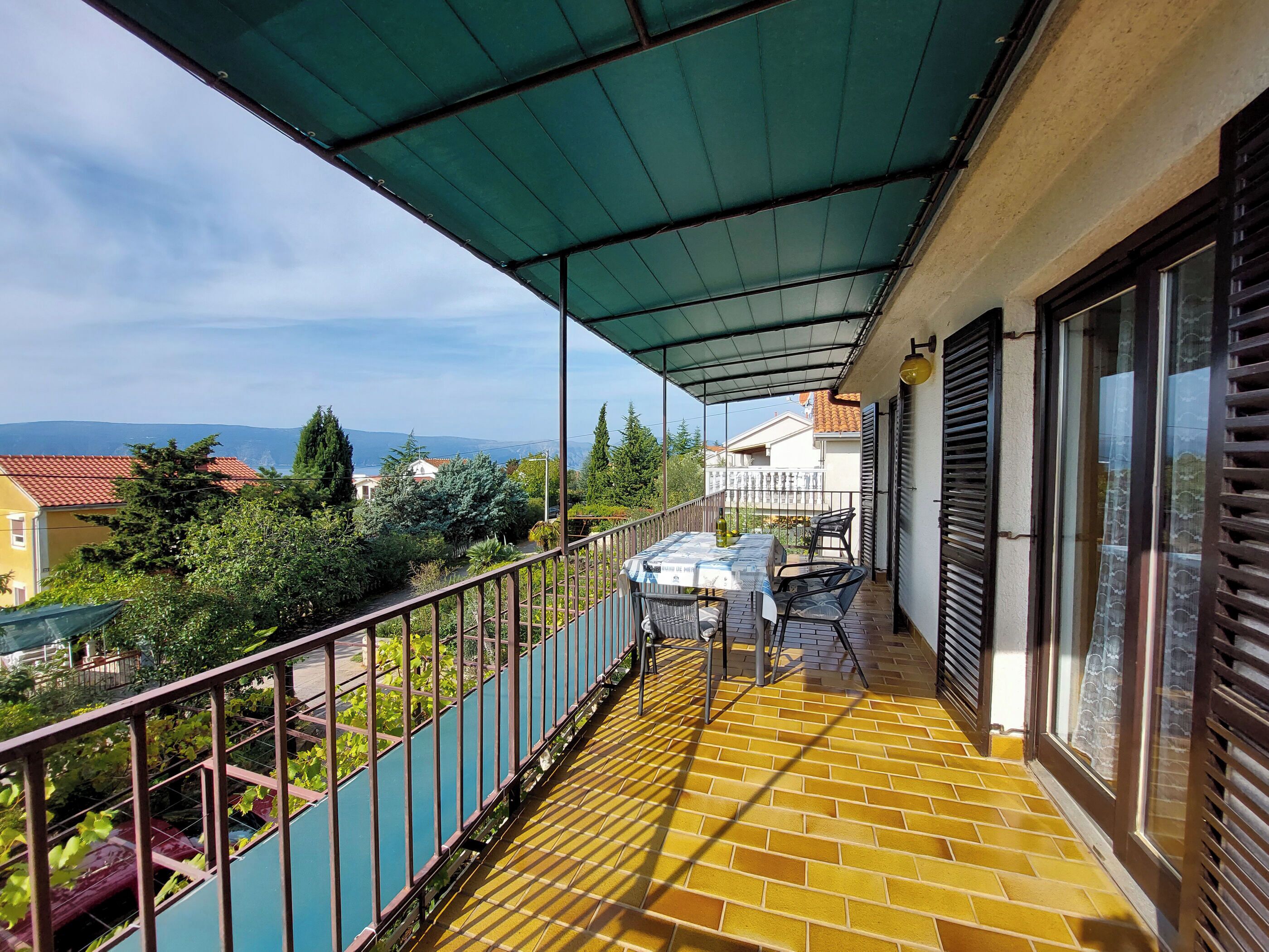 A balcony with a table and chairs, a covered area, and a view of the surrounding landscape.
