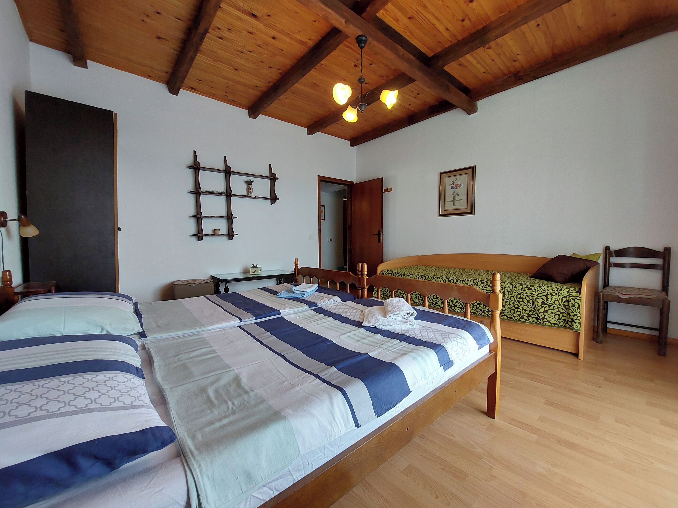 Quarto com duas camas, vigas de madeira no teto, uma mesinha e uma cadeira.