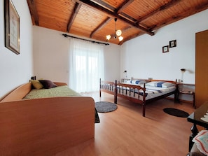 A bedroom with two beds, a wooden ceiling, and a large window with sheer curtains. - Apartments Vilim (Krk)