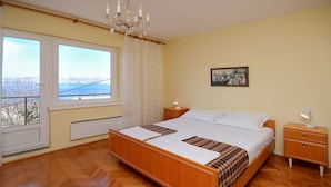 A bedroom with a wooden bed, two bedside tables, a chandelier, a window with a view, and a painting on the wall. - Apartment Milan (Senj)