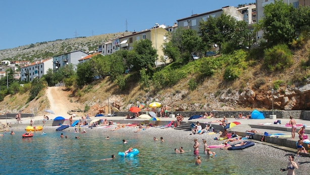 A beach with clear water, people swimming and sunbathing, and buildings in the background. - Apartment Milan (Senj)