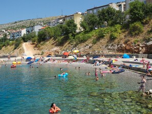 A beach with clear water, people swimming and sunbathing, and buildings in the background. - Apartment Milan (Senj)