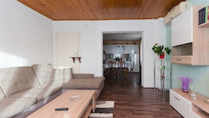 A living room with a wooden ceiling, a sofa, a coffee table, and a kitchen in the background. - Apartment Milan (Senj)