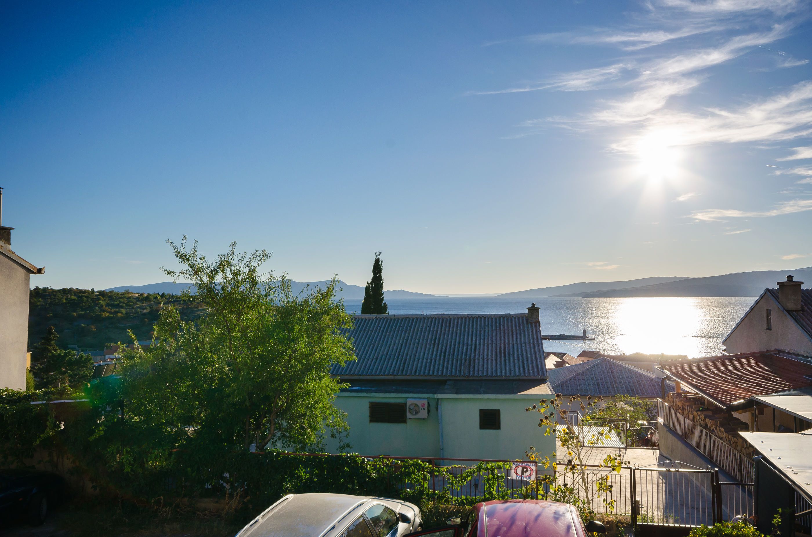 A coastal residential area with houses, a parked car, and a view of the sea.