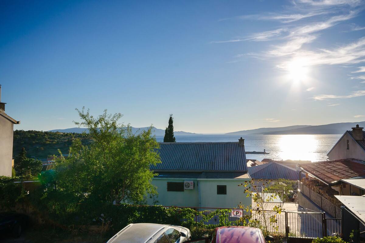 A coastal residential area with houses, a parked car, and a view of the sea.