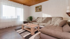 A living room with a wooden ceiling, a beige sofa, a coffee table, and a large window with sheer curtains. - Apartment Milan (Senj)