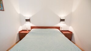 Ein ordentlich bezogenes Bett mit einem geometrisch gemusterten Überwurf, zwei Nachttische mit Lampen und ein hölzernes Kopfteil.