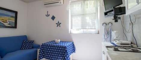 A room with a blue sofa, a table with a blue tablecloth, a TV mounted on the wall, and a stove.