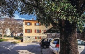 A two-story building with a stone facade, a parked car, and a tree in the foreground. - Apartment Nika (Tribalj)