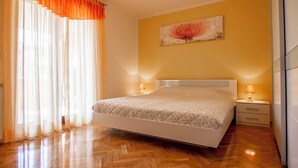 A bedroom with a bed, wooden flooring, a nightstand, a lamp, and a wall-mounted painting. - Apartments Edo (Stinjan)