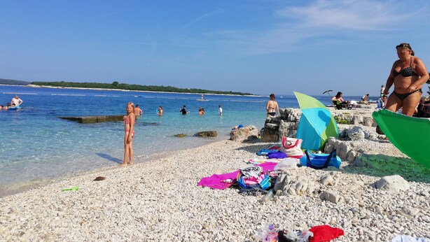 A pebbled beach with clear water, people swimming, and some beach umbrellas. - Apartments Edo (Stinjan)