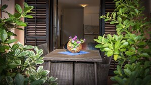 A dining table with a wicker chair, a wicker basket with flowers, and a view of a kitchen and dining area through an open door. - Apartments Edo (Stinjan)