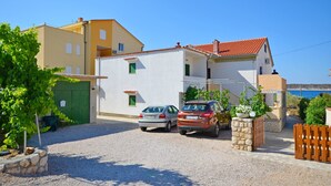 Ein zweistöckiges Haus mit Kiesweg, geparkten Autos und Blick auf das Meer.
