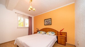 Ein Schlafzimmer mit Bett, Holzkopfstück, Nachttischen, einem Fenster mit Vorhängen und einer Deckenleuchte.