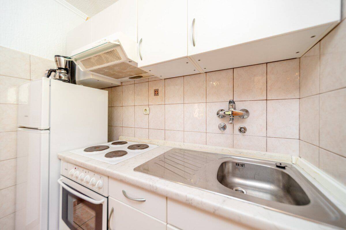 A compact kitchen with white cabinetry, a built-in stove, a sink, and a coffee maker on the countertop.
