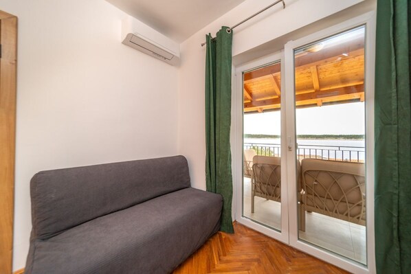 Une pièce avec un canapé gris, un plancher en bois, une porte-fenêtre coulissante donnant sur un balcon extérieur doté d’un plafond en bois et de deux chaises.