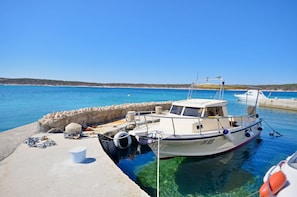 A boat docked at a pier with clear blue water and a distant shoreline. - Apartments Marinko (Barbat)