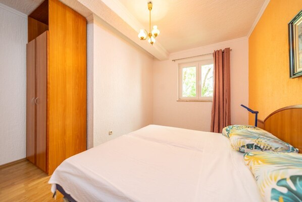 A bedroom with a bed, a window with curtains, a wardrobe, and a chandelier. - Apartments Marinko (Barbat)