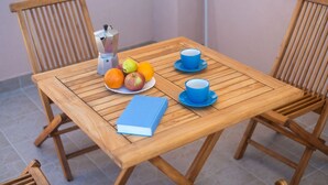 Ett träbord med en tallrik frukt, två blå koppar, en bok och en kaffebryggare.