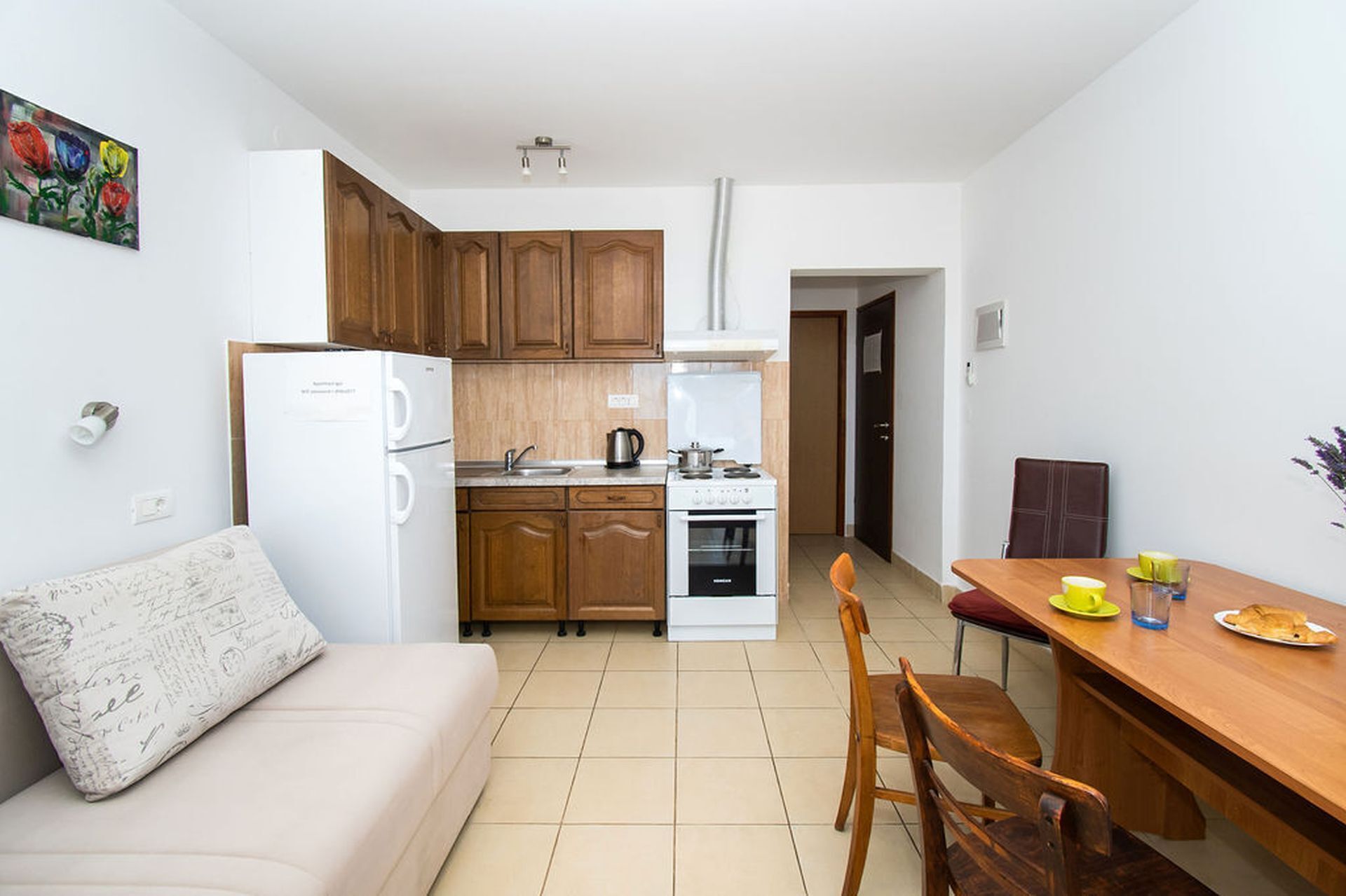 A compact kitchen with a refrigerator, stove, and sink, a dining table with chairs, and a sofa.