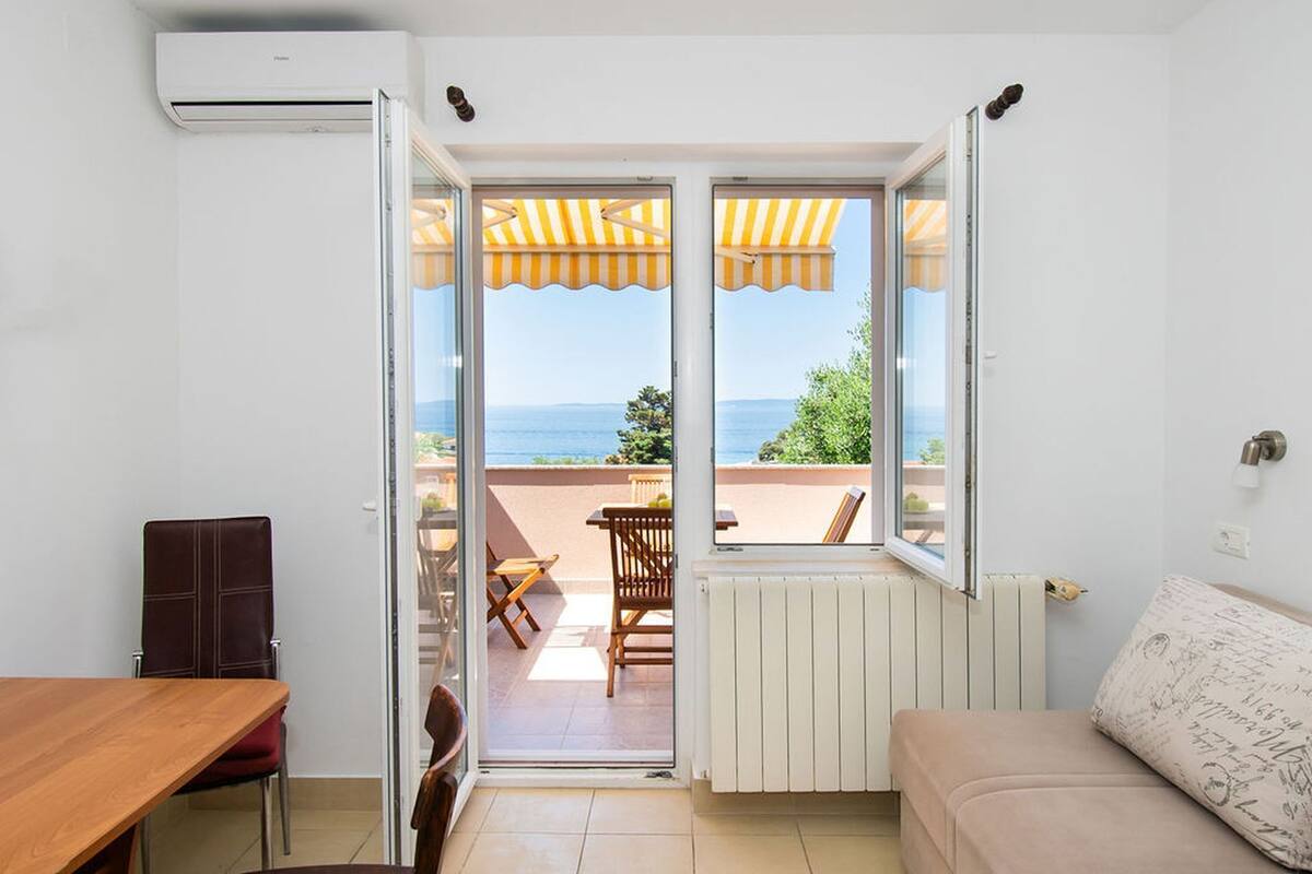 Une pièce dotée d’une porte-fenêtre coulissante donnant sur un espace extérieur aménagé avec une table et des chaises, un radiateur et un canapé.