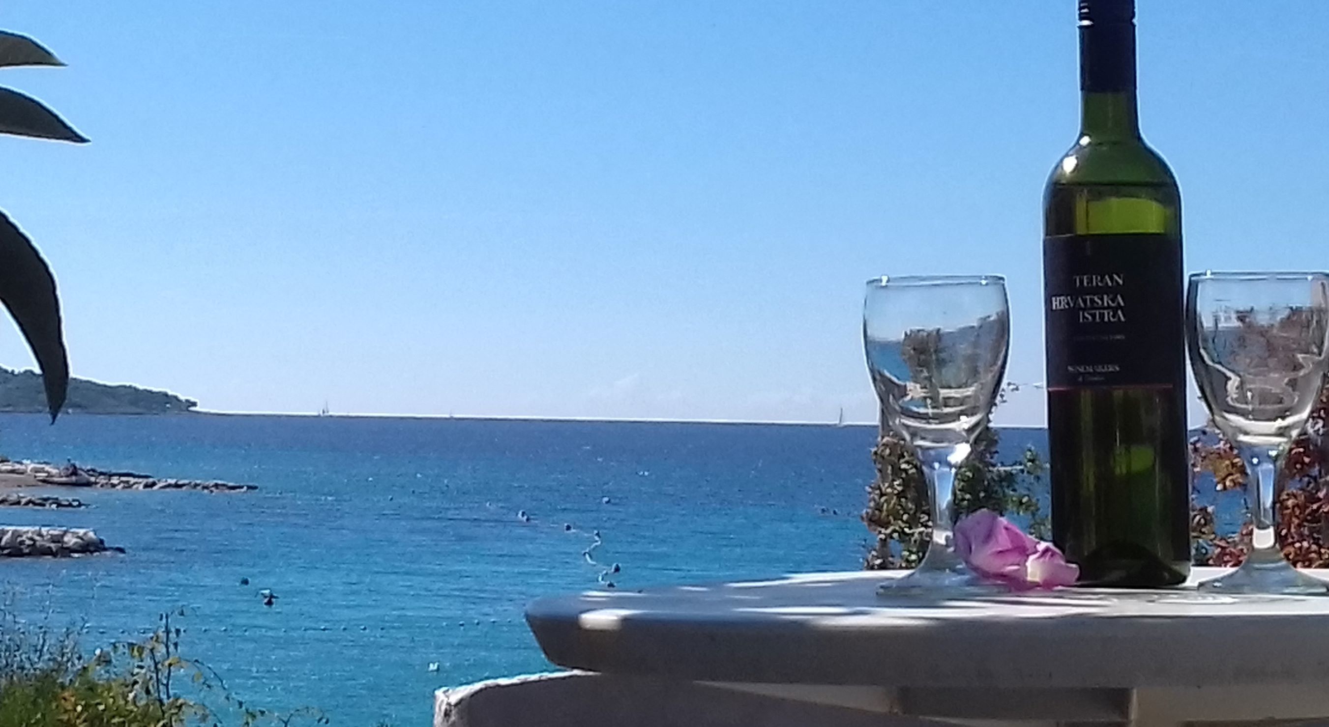Una mesa con una botella y dos vasos junto al mar.
