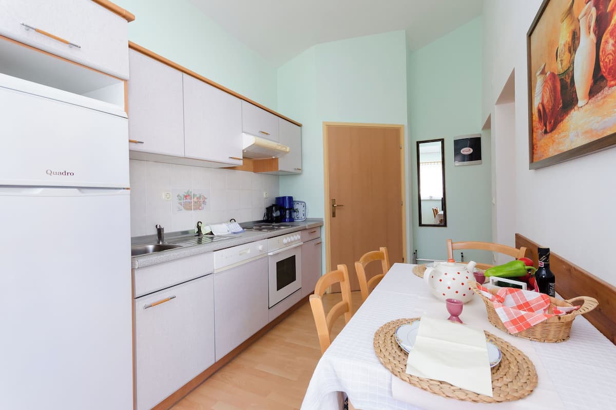 A compact kitchen with white cabinets, a coffee maker, and a dining table set with a placemat, a teapot, and a basket.