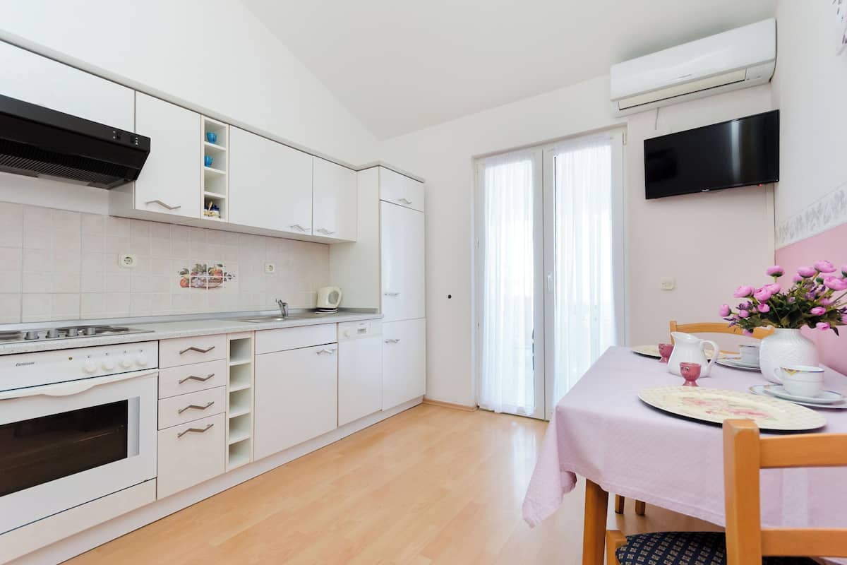 A modern kitchen with white cabinets, a built-in oven, and a dining area with a pink tablecloth.