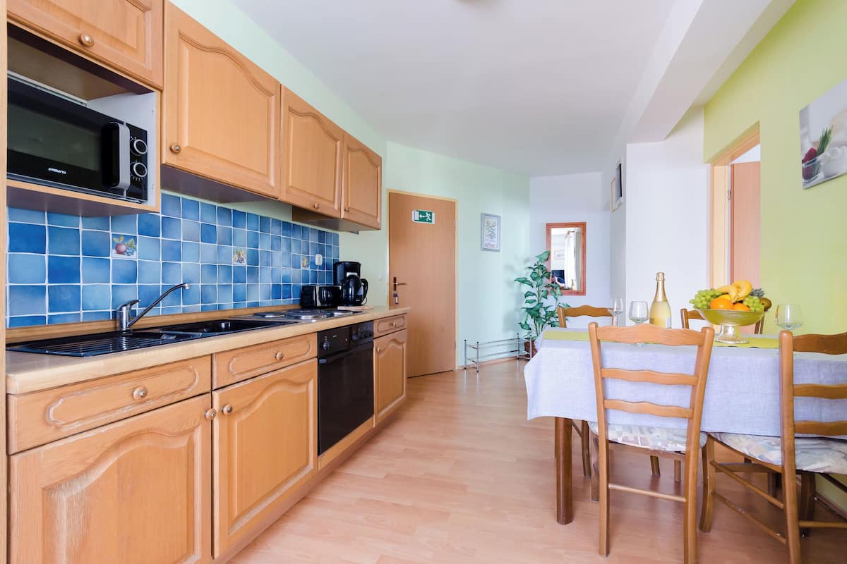 A kitchen with wooden cabinets, a microwave, and a coffee maker. There is a dining table with chairs and a fruit bowl.
